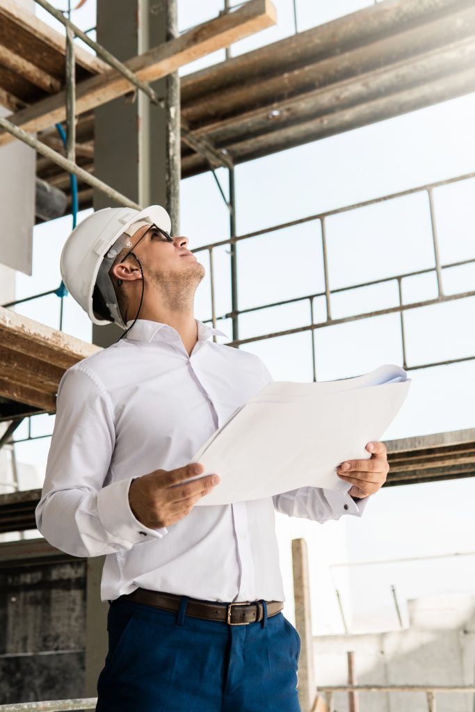 young man architect businessman wearing hard hat holding blueprints construction site
